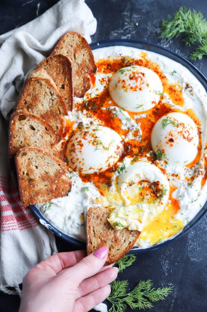 Hand holding bread slice in turkish eggs image