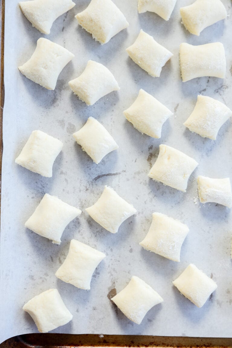 Rows of uncooked gnocchi di ricotta are arranged on a parchment-lined baking sheet, ready for cooking. The delicate gnocchi are lightly dusted with flour and evenly spaced on the tray.