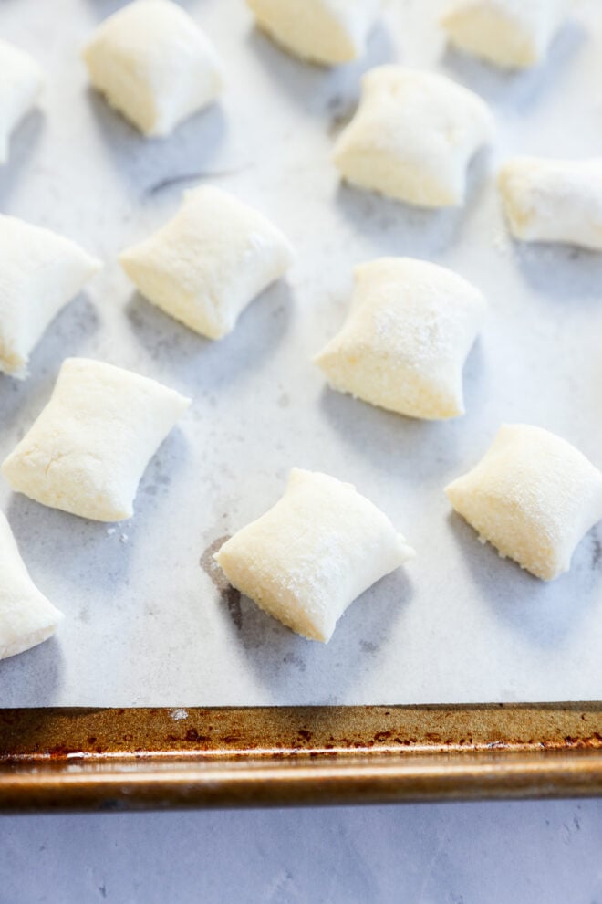 Raw gnocchi di ricotta pieces arranged on a parchment-lined baking sheet, ready to be cooked. The dough pieces are lightly floured and evenly spaced on the tray.