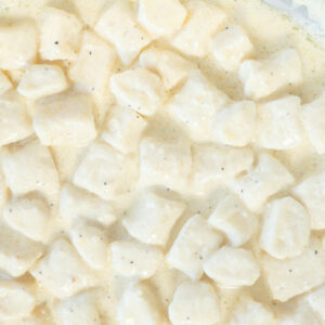 Close-up of gnocchi di ricotta pasta coated in a creamy white sauce with visible black pepper specks.