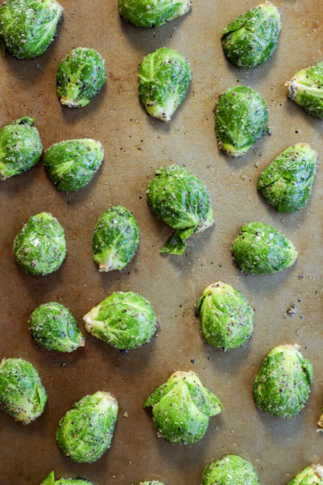 Brussels sprouts coated with seasoning and arranged in rows on a baking sheet, ready to be roasted.