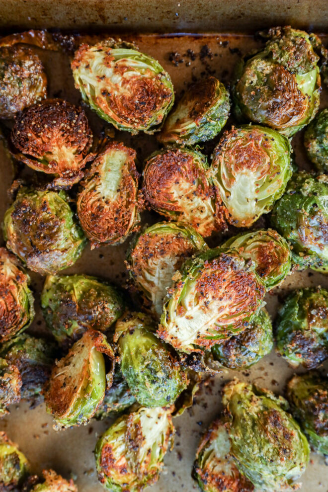 Roasted Brussels sprouts are cut in half and baked on a tray, showing browned, crispy edges and a lightly seasoned surface.