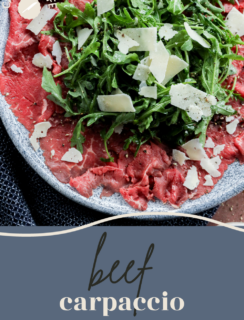 A plate of Carpaccio di Manzo topped with arugula and shaved Parmesan cheese sits on a dark surface. The words beef carpaccio are written on a blue-gray background below the plate.