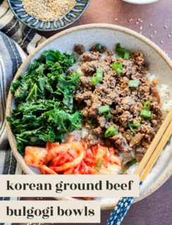 A bowl filled with ground beef topped with chopped green onions, steamed kale, kimchi, and white rice, served with chopsticks. Sesame seeds and green onions are visible in small bowls nearby. Text reads: korean ground beef bulgogi bowls.