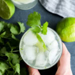 hand holding a cocktail with cilantro and lime