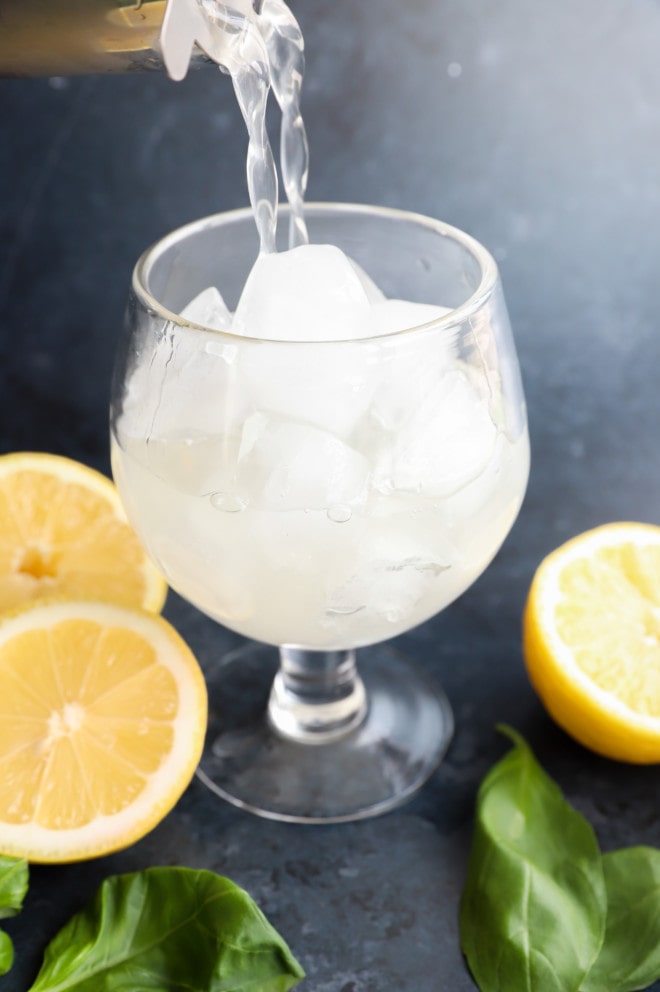 Pouring into glass lemon drink with fresh herbs