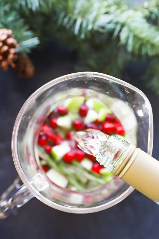 pouring white wine into a pitcher for a holiday cocktail