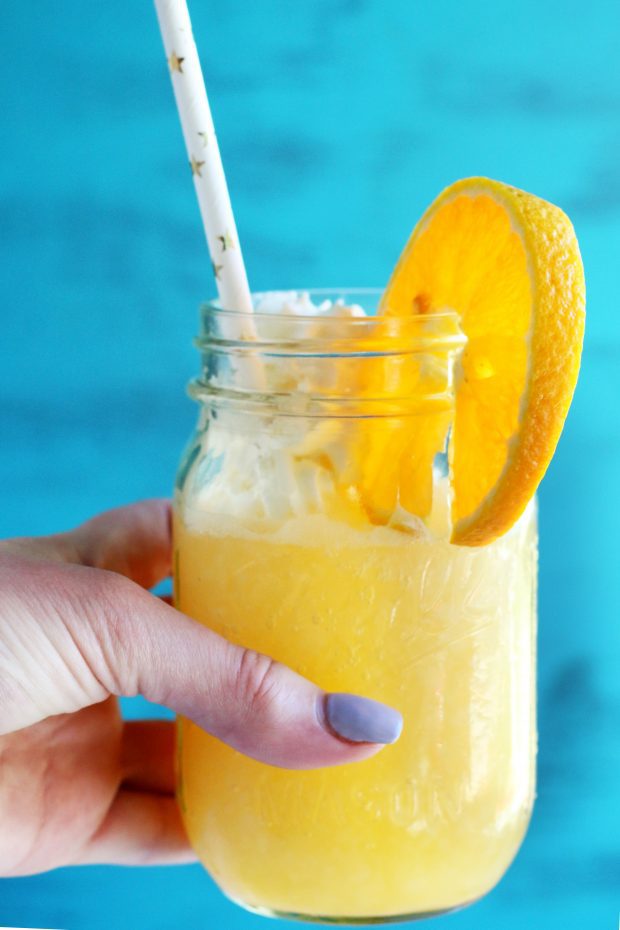 Hand holding an orange dreamsicle with orange and whipped cream