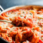 spoon lifting out italian penne dish with poultry and marinara sauce and cheese