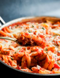 spoon lifting out italian penne dish with poultry and marinara sauce and cheese