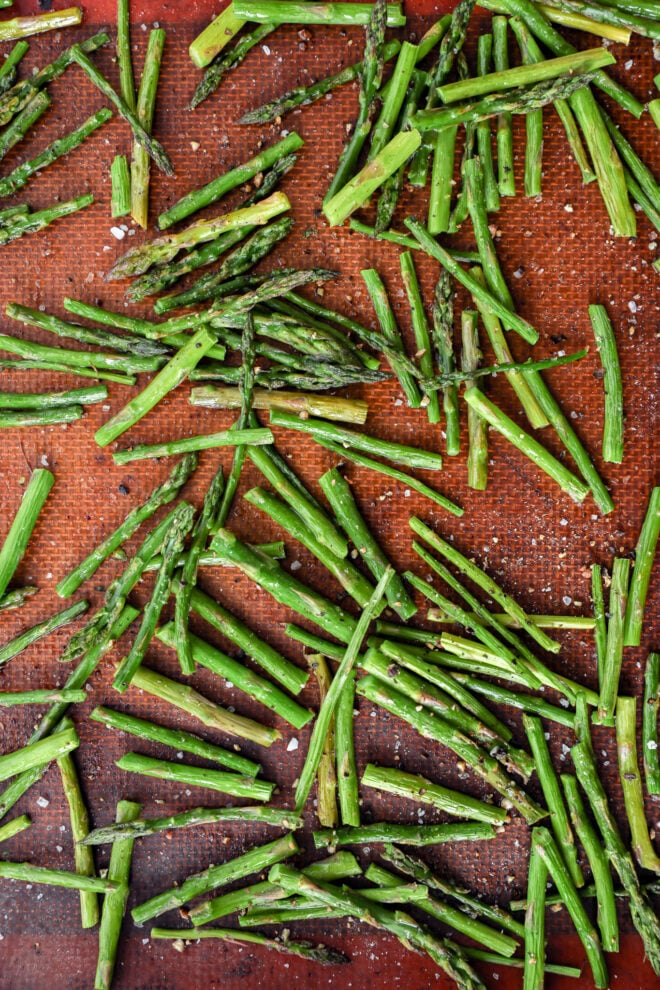 Chopped asparagus spears spread out on a baking sheet, sprinkled with coarse salt.