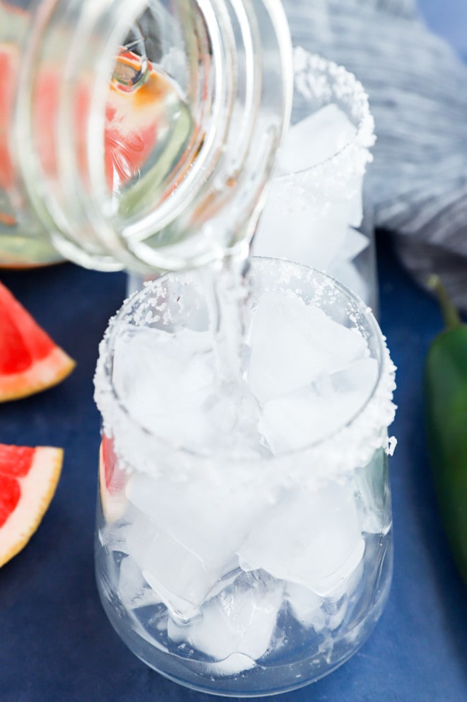 Pouring infused vodka or gin into a cocktail glass filled with ice