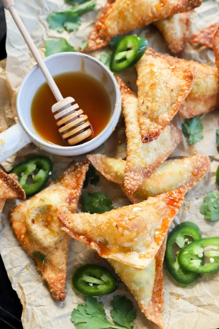 Overhead image of wontons on a baking sheet with hot honey and jalapeños