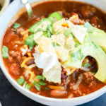 Spicy taco chili in a bowl with avocado, sour cream, and cheese