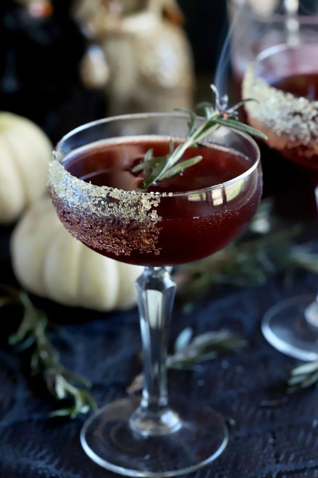 Spooky Pomegranate Cocktail on the table with pumpkins and rosemary