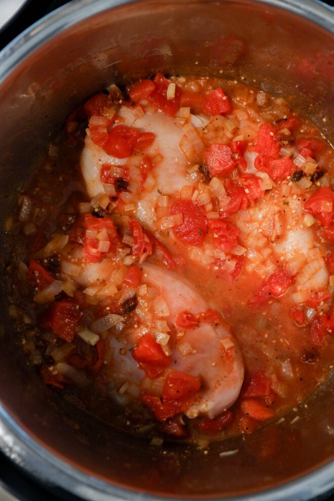 Two raw chicken breasts topped with chopped tomatoes, onions, and seasonings are cooking in a metal pot.