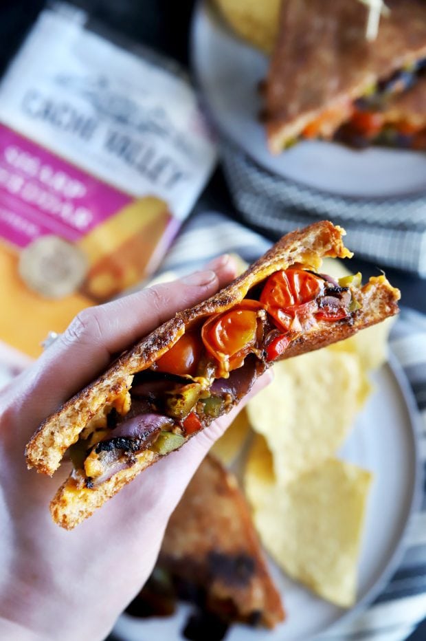 Holding half of a grilled cheese sandwich with grilled vegetables