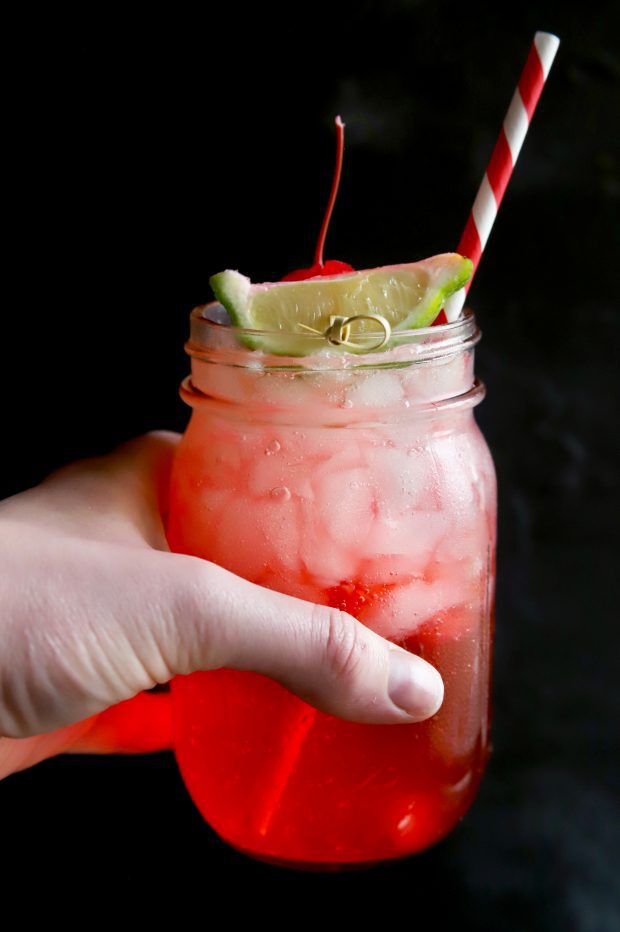 Holding a bubbly cherry and lime cocktail in a mason jar