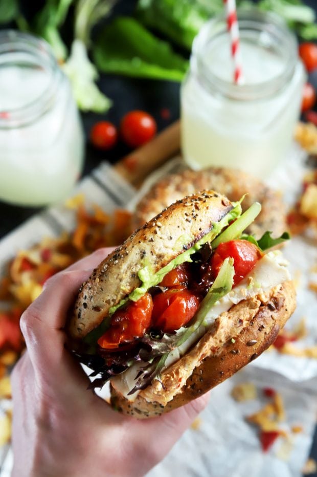 Hand holding a bagel sandwich with turkey and vegetables