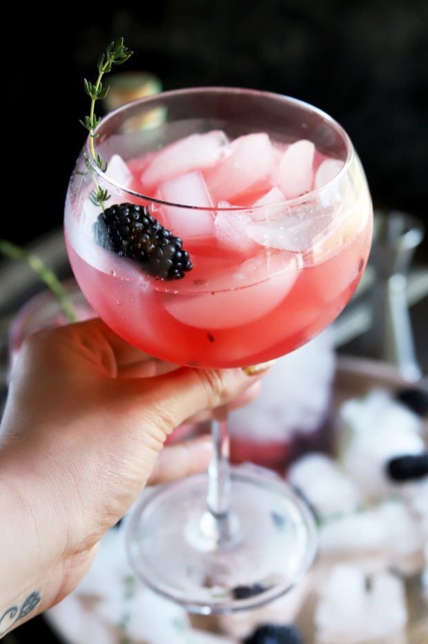 Holding a gin cocktail with blackberry and thyme