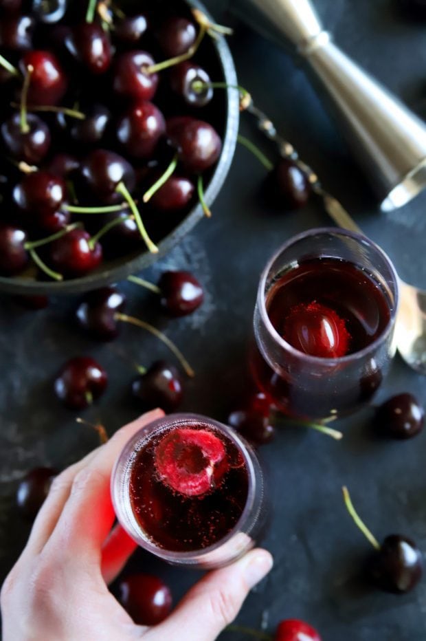 Overhead shot of picking up a champagne flute with fresh cherries and rose mimosa