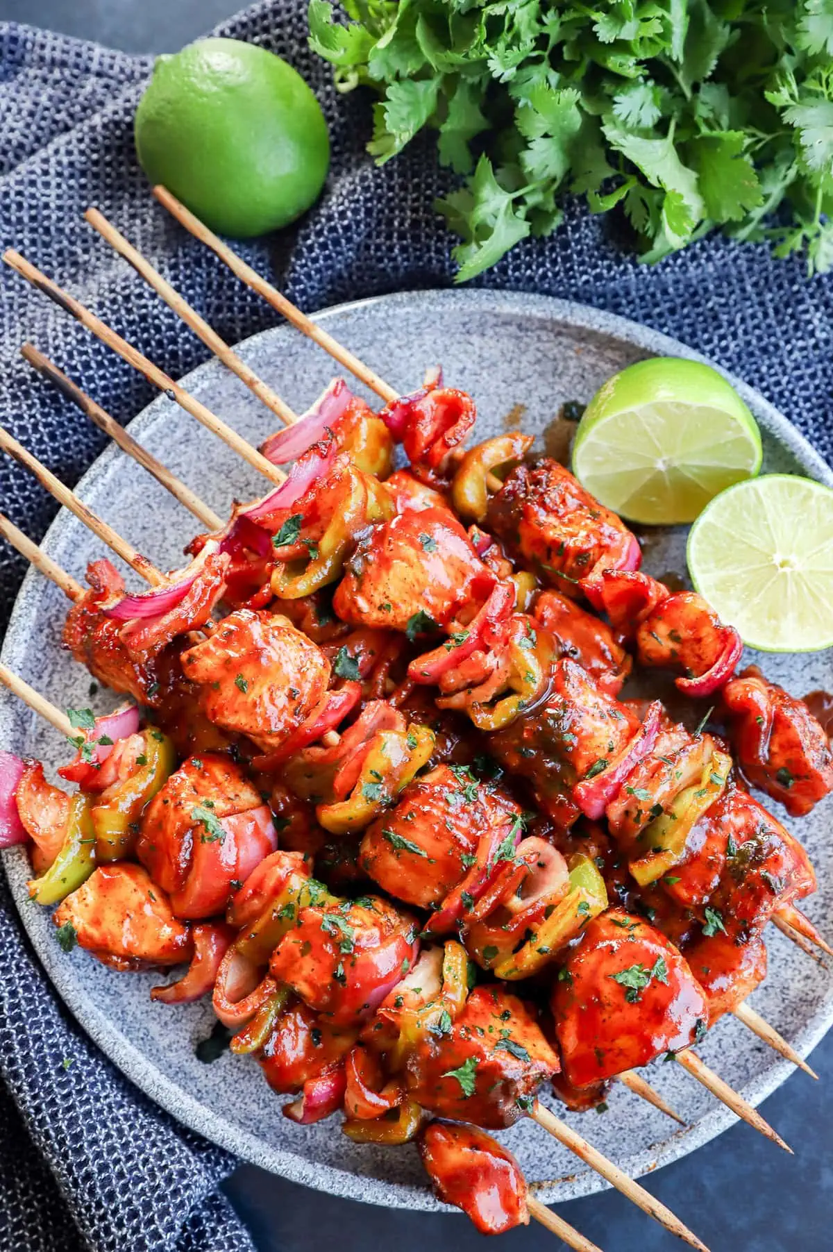 Plate of grilled bbq chicken kabobs with lime halves and cilantro bunch