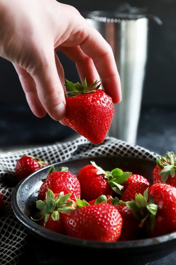 Hand picking up a strawberry out of a bowl of berries