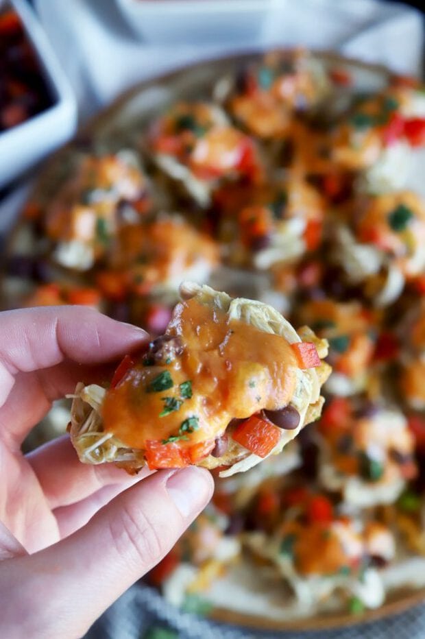 Hand holding an individual nacho with chicken and vegetables