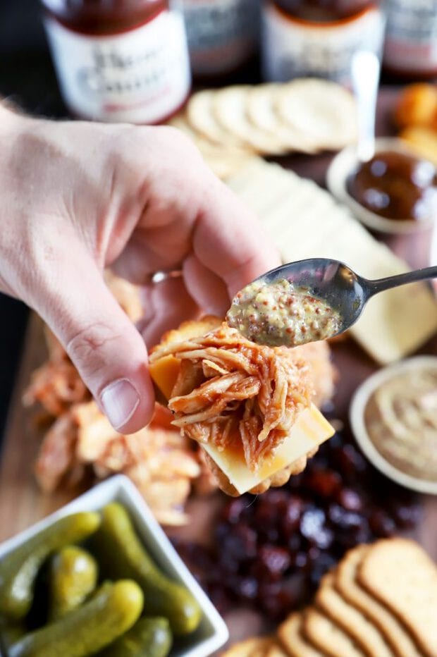 Spooning mustard over BBQ meat on a cracker