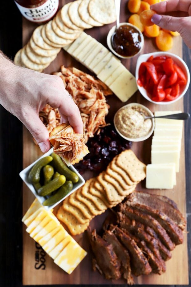 Holding a cracker with BBQ meat and cheese