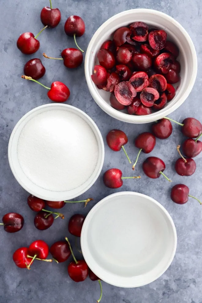 cherries in a bowl, sugar in a bowl, and water in a bowl plus fresh cherries