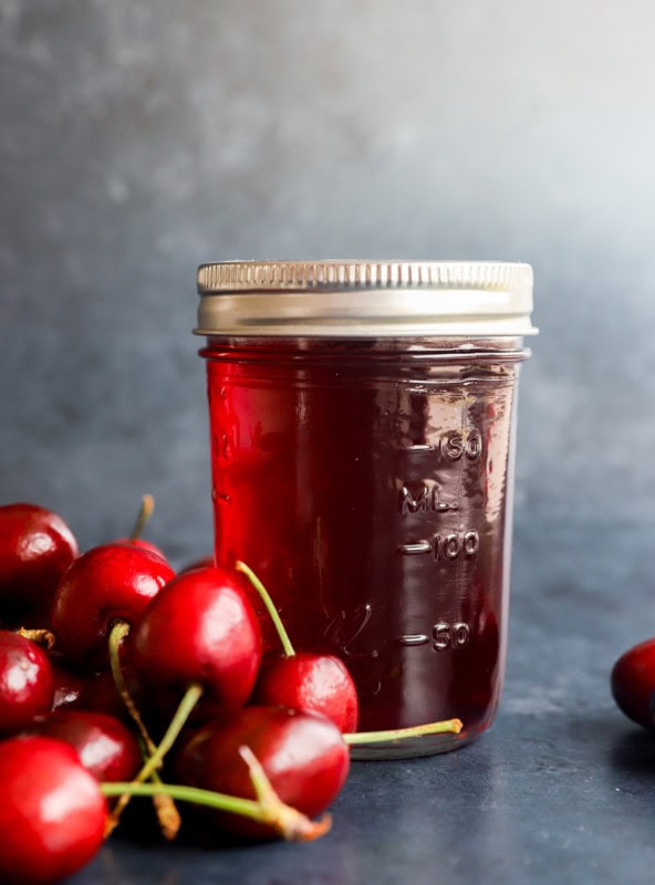 flavored syrup in a jar with fresh cherries in a pile