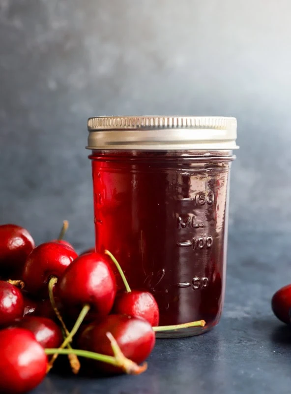 flavored syrup in a jar with fresh cherries in a pile