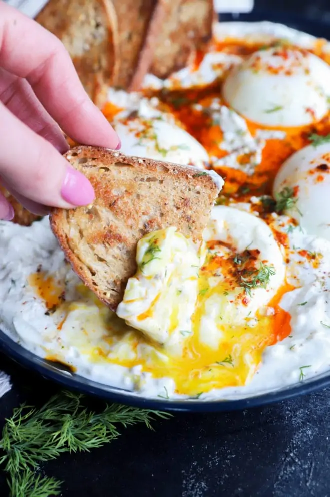 Hand dipping bread into yogurt and poached eggs image
