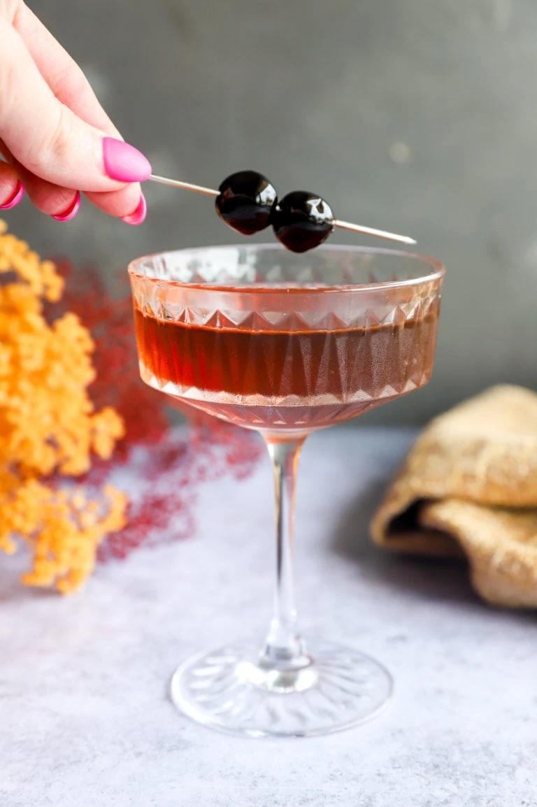 Adding a cherry garnish to a coupe glass