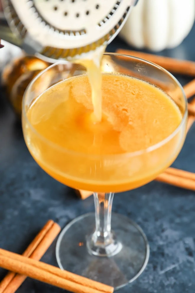 Straining a pumpkin fall cocktail into a glass