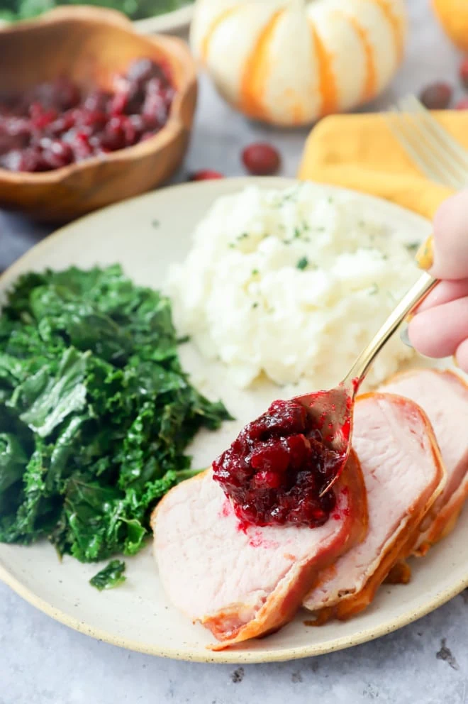 spooning cranberries onto bacon wrapped pork tenderloin