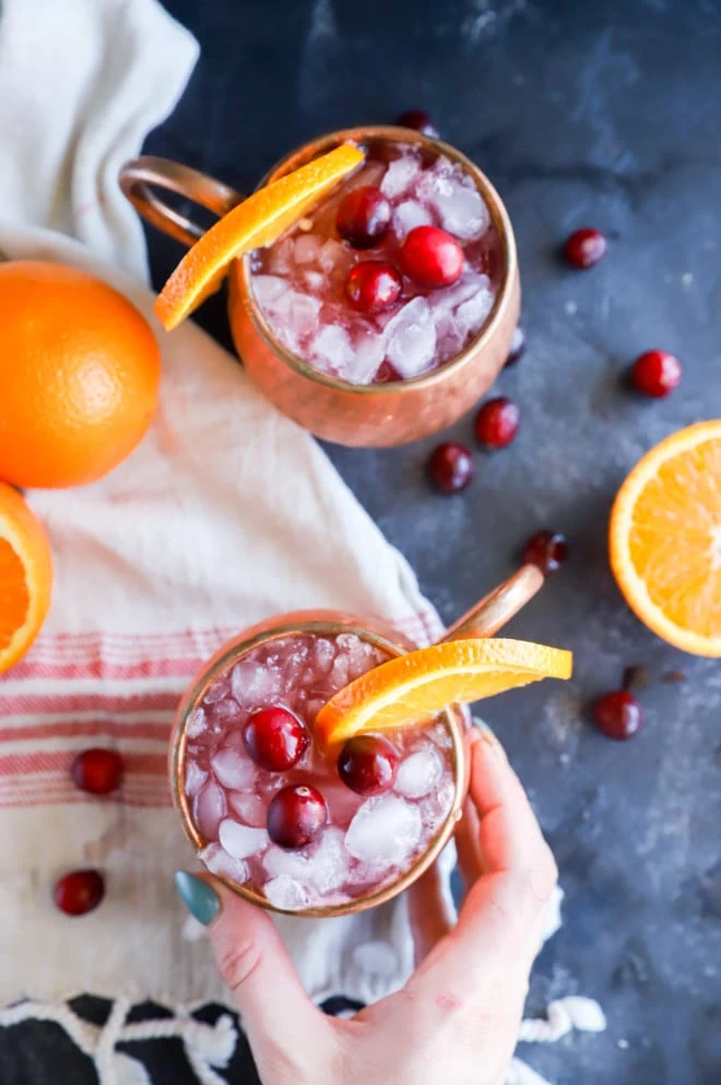 Hand holding a moscow mule mug with orange and cranberries