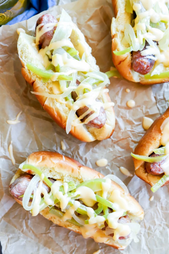 Grilled brats on paper with vegetables and cheese sauce