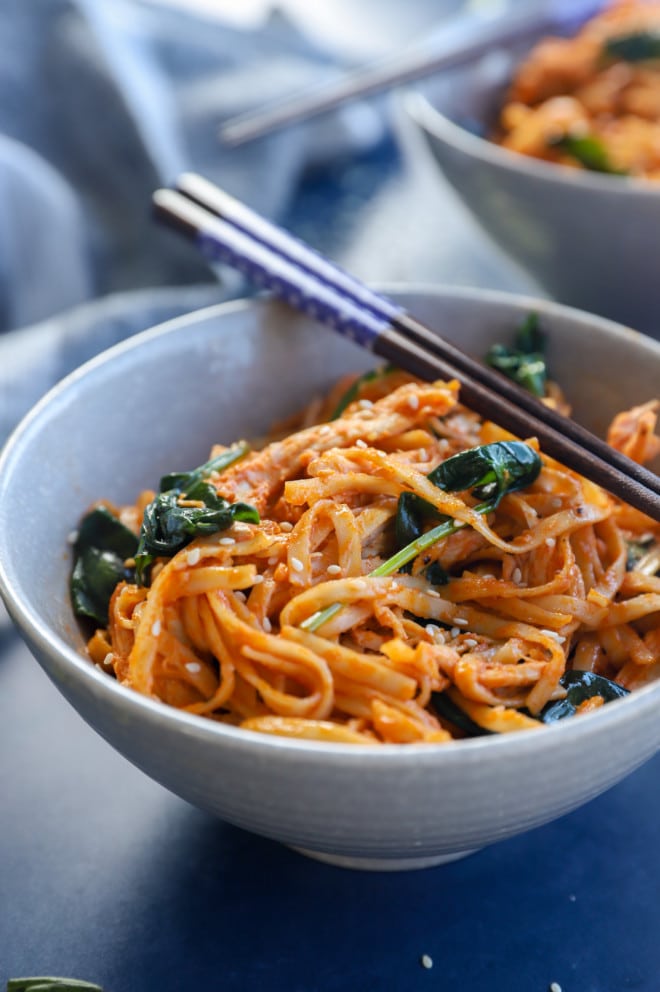 Gochujang noodles in a bowl with chopsticks and chicken and spinach