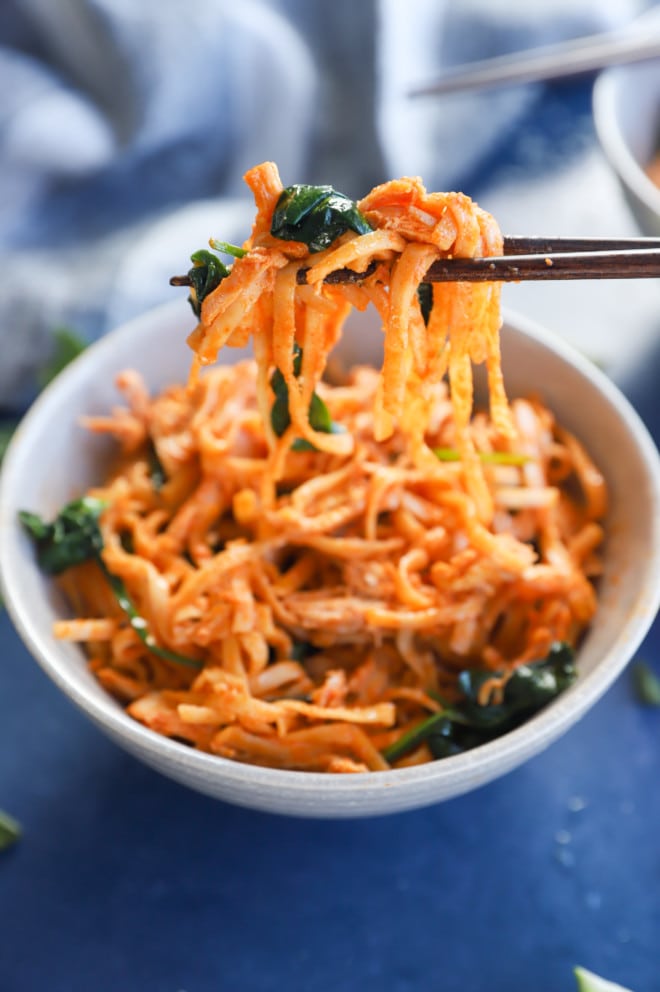 Chopsticks holding korean noodles and a bowl picture