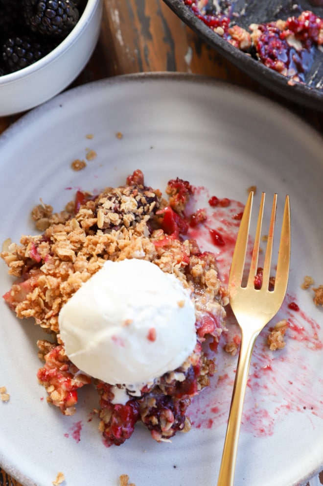 Overhead photo of apple blackberry crumble on plate with fork and ice cream