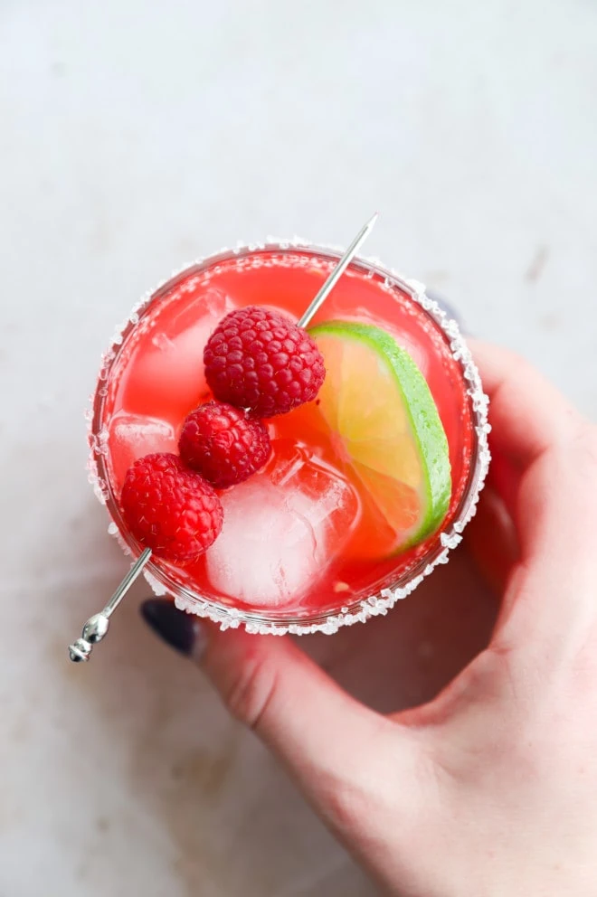 Hand holding a raspberry margarita in a glass image