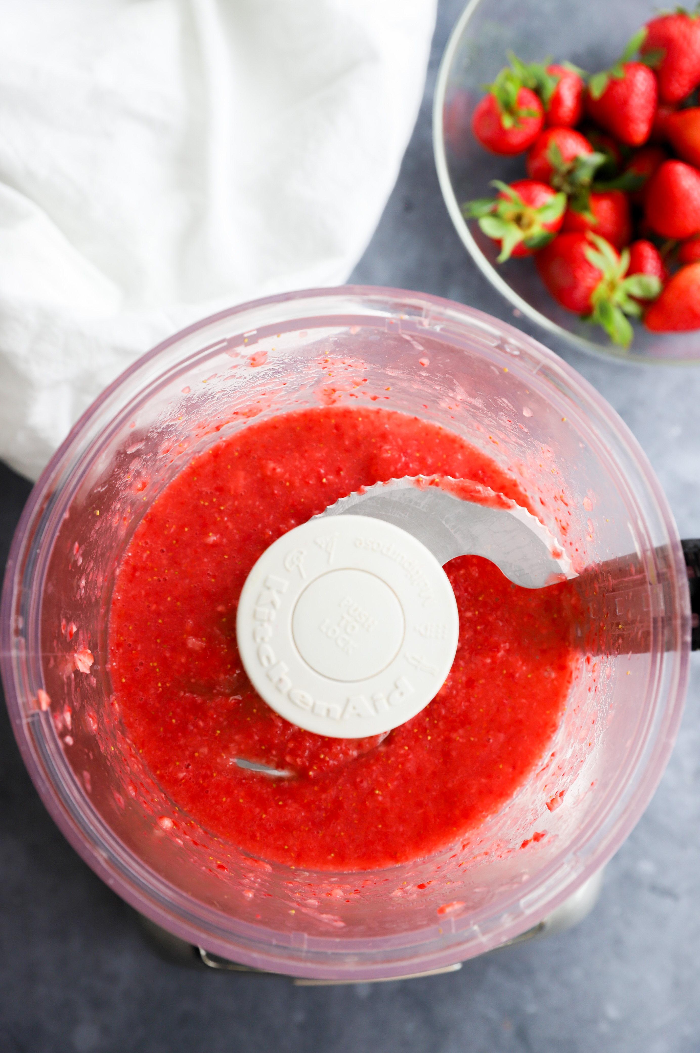 strawberry puree in a food processor with fresh berries in a bowl