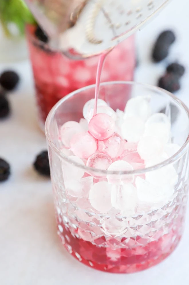 Pouring blackberry gin mixture into glass with ice image