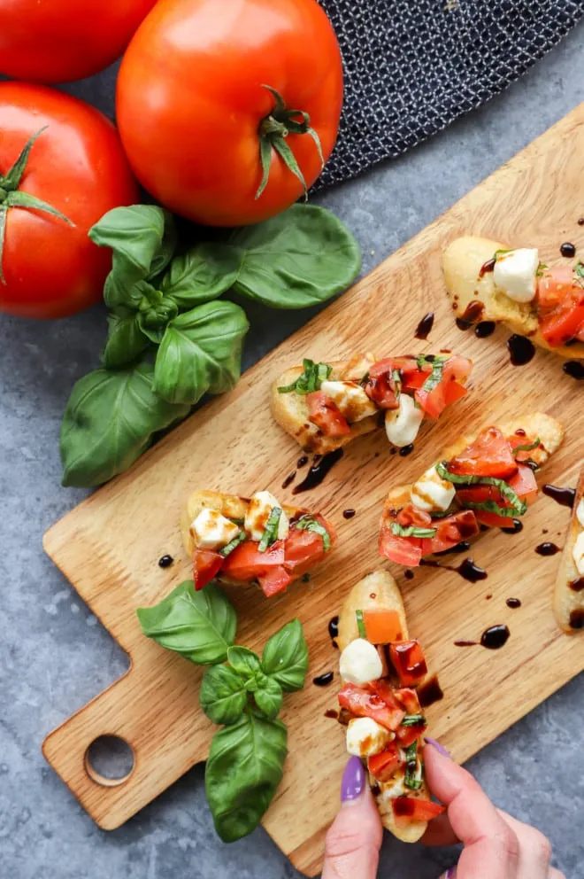 Overhead image of caprese bruschetta on platter with hand holding piece