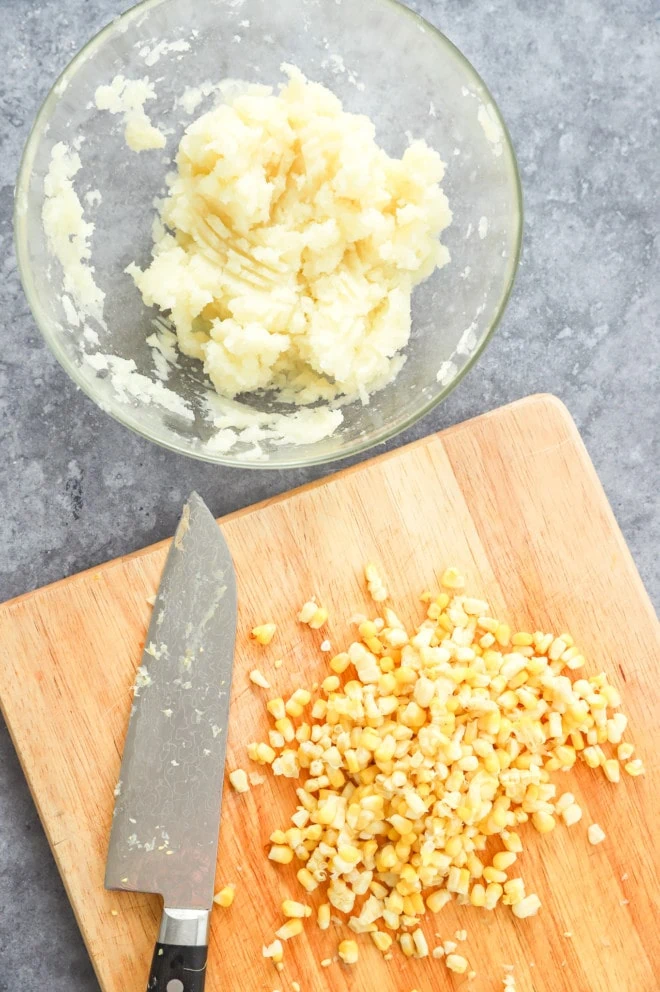 Mashed potato in a bowl with corn kernels on cutting board image