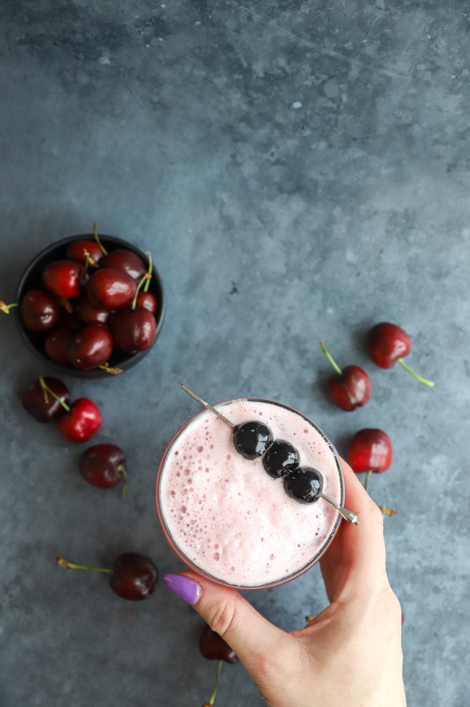 Hand holding summer cocktail with cherries