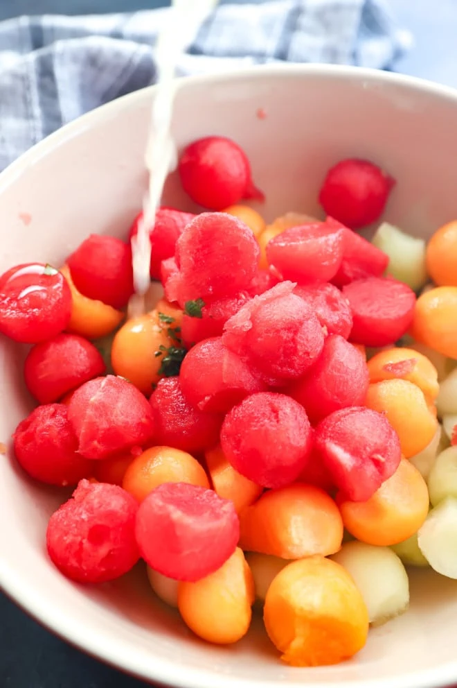 Pouring on dressing onto fruit in bowl