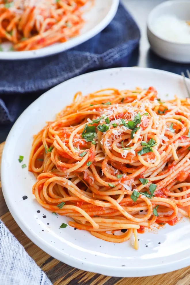 Pile of spaghetti with tomatoes on a plate with a bowl of cheese